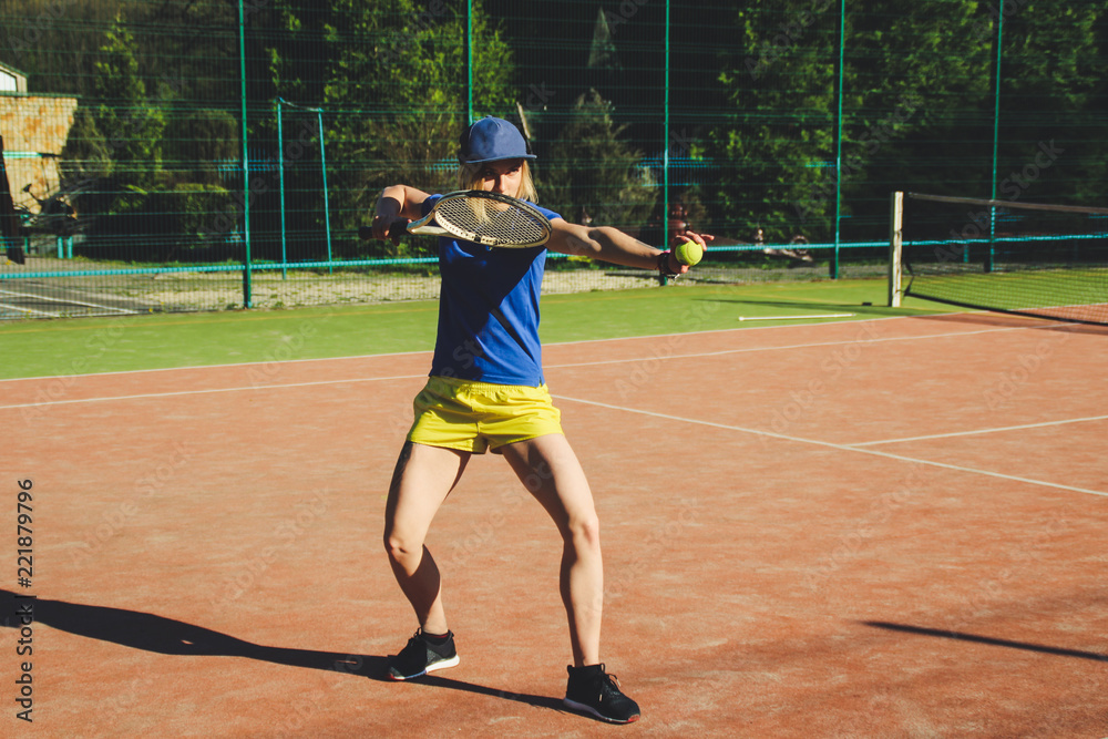 Portrait of a blonde girl with a short haircut. Background tennis court. Dark blue t-shirt polo and yellow shorts.Sport shooting.