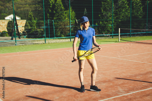 Portrait of a blonde girl with a short haircut. Background tennis court. Dark blue t-shirt polo and yellow shorts.Sport shooting. © Yaroslav
