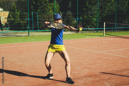 Portrait of a blonde girl with a short haircut. Background tennis court. Dark blue t-shirt polo and yellow shorts.Sport shooting. © Yaroslav