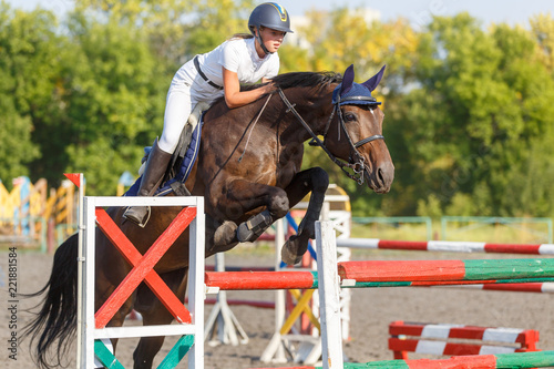 Young horse rider girl jumping over a hurdle on show jumping competition © skumer
