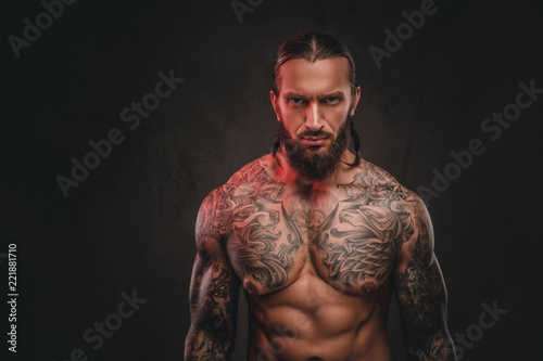 Close-up photo of a brutal shirtless bearded tattooed male. Isolated on a dark textured background.