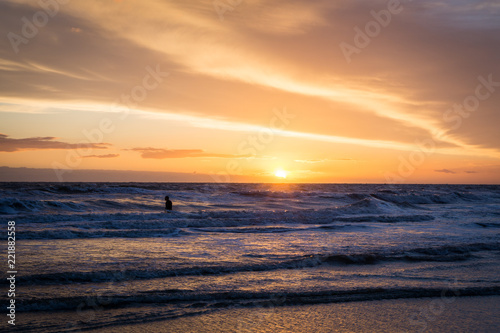 silhouette of a surfer standing in water at the beach during sunset