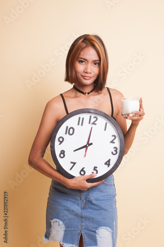 Healthy Asian woman drinking glass of milk hold clock.