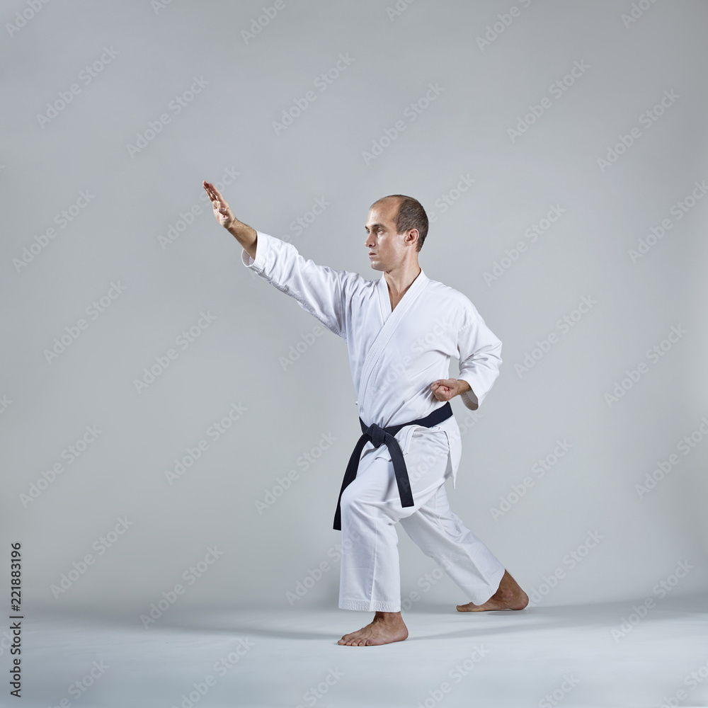 On a gray background, an adult sportsman trains a formal karate exercise