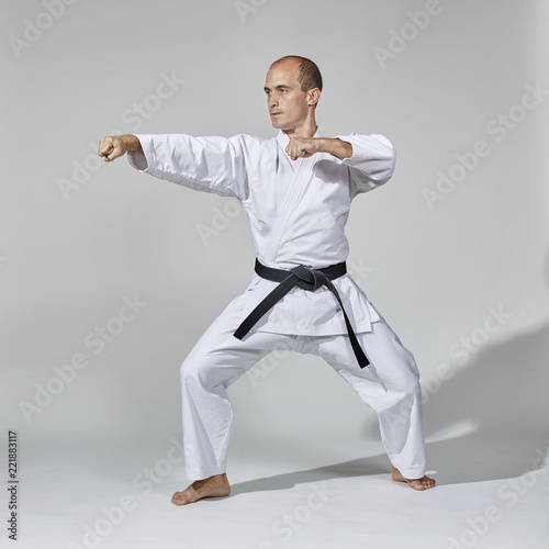 On a gray background, a young athlete performs formal karate exercises