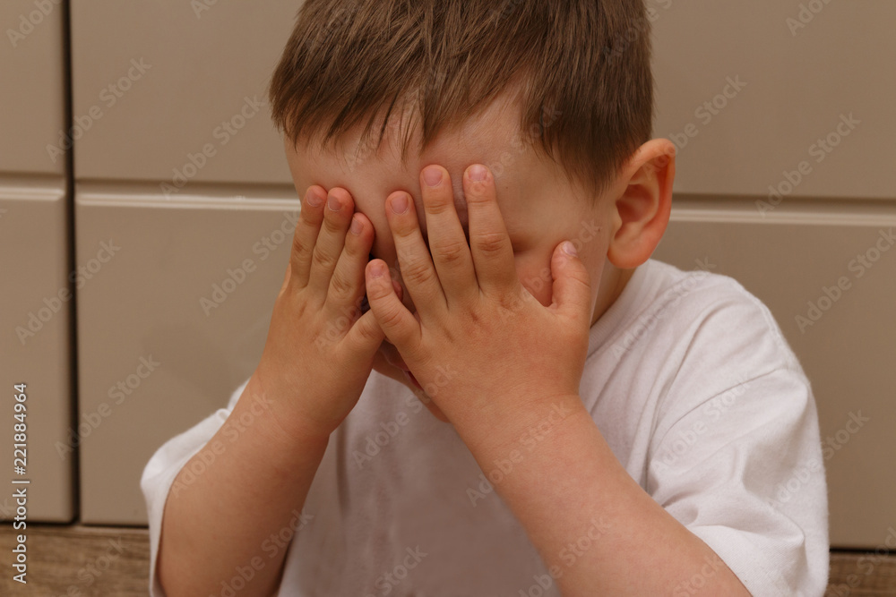 the boy in the white T-shirt closed his eyes with his hands. hiding, crying, frightened. the boy in the white T-shirt closed his eyes with his hands. hiding, crying, frightened.