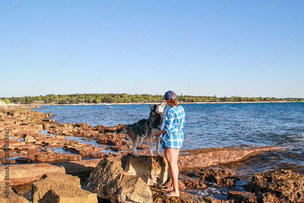 Adriatic sea view.Husky play on sea stones beach. Girl play with dog and him food. Treveling with dog.Croatia