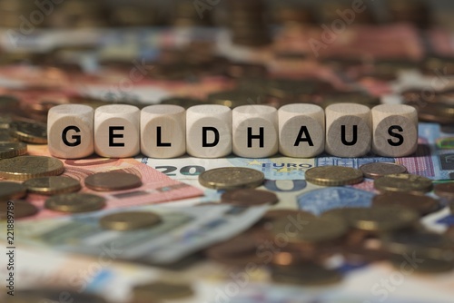 Geldhaus - Holzwürfel mit Buchstaben bedruckt im Hintergrund liegen Banknote und Kleingeld