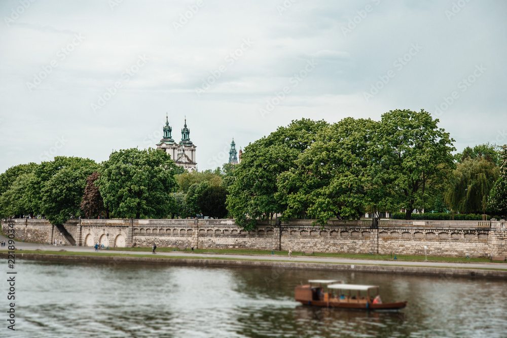 Fototapeta premium The river flows through the city. Church on the hill above the river. Wisla River in Krakow. Float the boat and the ship under water