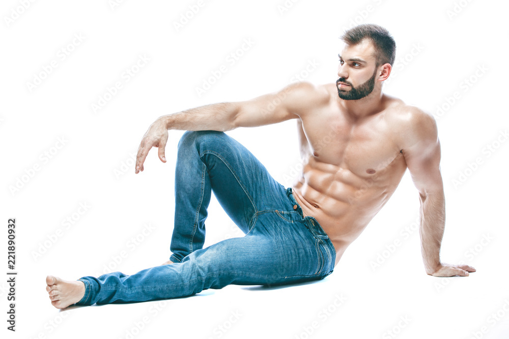 bodybuilder posing. Beautiful sporty guy male power. Fitness muscled in blue jeans. on isolated white background. sits on the floor bodybuilder posing. Beautiful sporty guy male power. Fitness muscled in blue jeans. on isolated white background. sits on the floor