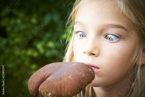 Child blong girl posing in forest and holding fresh picked mushroom  boletus . Selective focus