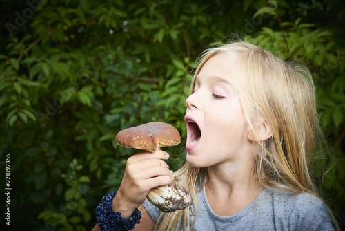 Child blong girl posing in forest and holding fresh picked mushroom (boletus). Selective focus photo