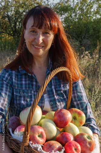 woman with red hair standing holding a basket of red apples on the garden background