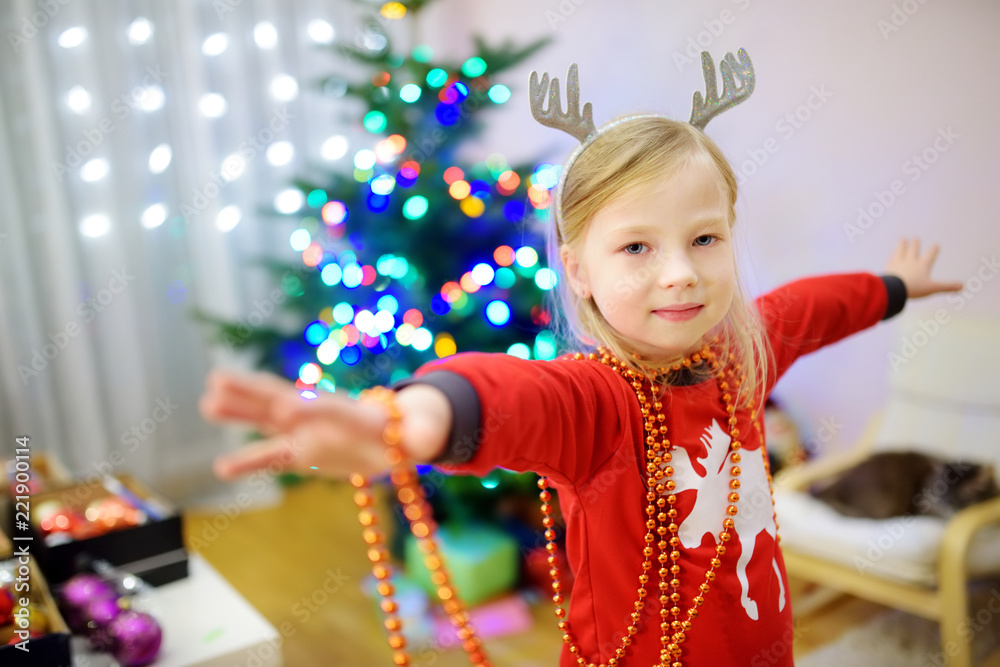 Adorable little girl decorating the Christmas tree with colorful glass baubles. Trimming the Christmas tree. Adorable little girl decorating the Christmas tree with colorful glass baubles. Trimming the Christmas tree.