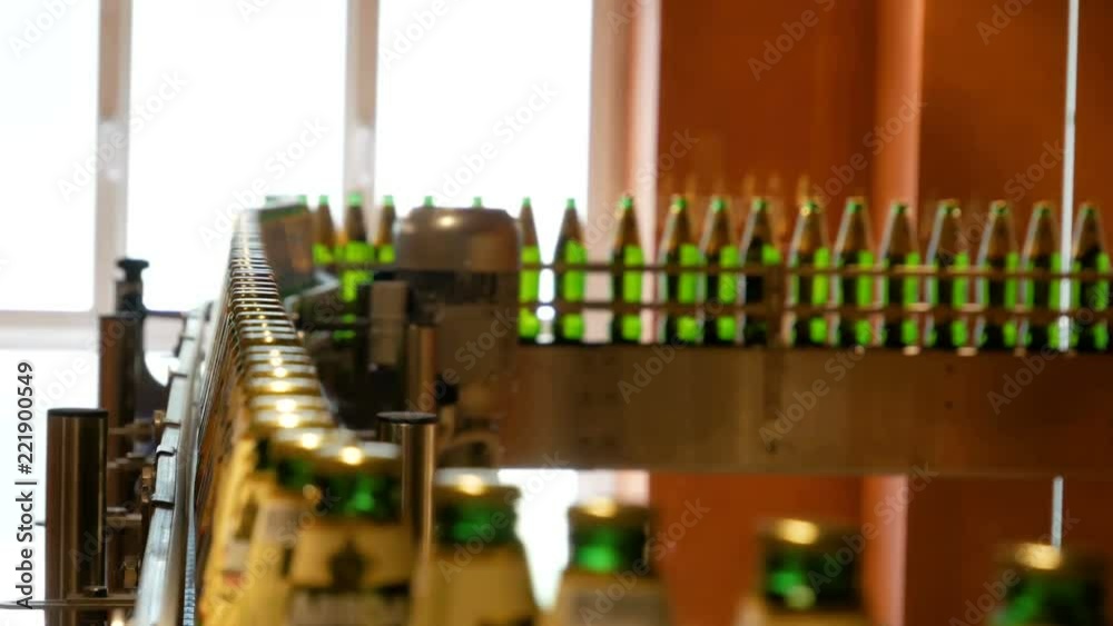 Large number of glass bottles with beer are moving along the conveyor. Low alcohol production. Drinks are ready to eat. Factory equipment at work. The finished product moves to another stage. Factory