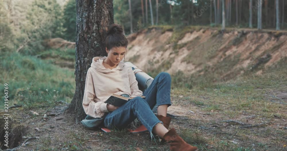 Attractive young woman reading a book outdoor in forest. Hiker camping in woods. 4K video shooting by handheld gimbal Attractive young woman reading a book outdoor in forest. Hiker camping in woods. 4K video shooting by handheld gimbal