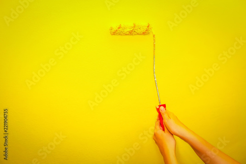 Female hand painting wall in yellow with paint roller. photo