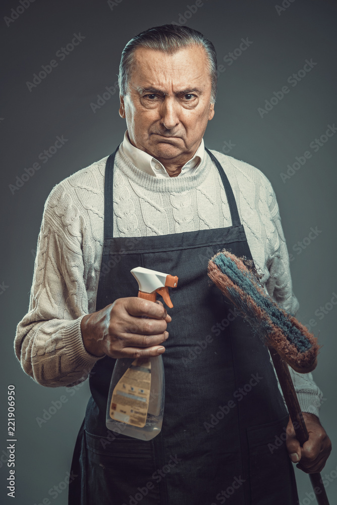 Senior old man disgusted by the idea of cleaning, holding cleaning  chemicals and wearing apron Stock Photo | Adobe Stock