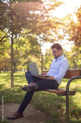 Handsome young businessman working on his laptop in the park