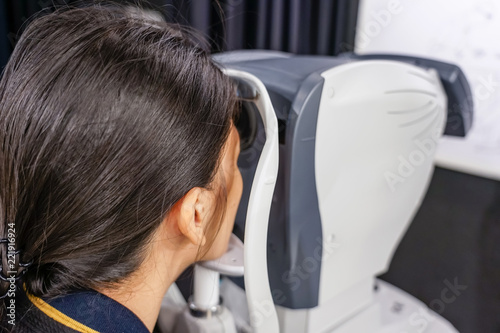 health care, medicine, people, eyesight and technology concept - Young woman checks his vision on the machine checking patient vision at eye clinic or optics store. face close-up