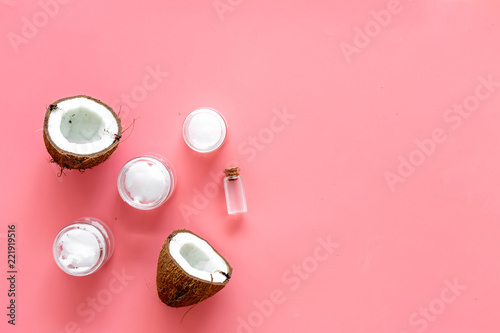 Cosmetics based on coconut oil. Oil in small bottle, cream, coconut pulp, half of coconut with shelf on pink background top view copy space