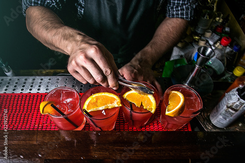 hands of the bartender who prepares red cocktails with orange slices  top view