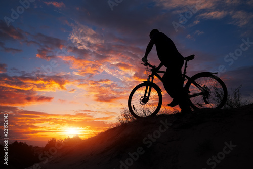 Fototapeta Naklejka Na Ścianę i Meble -  Silhouette of sports person cycling on the meadow on the beautiful sunset. Young man riding bicycle.