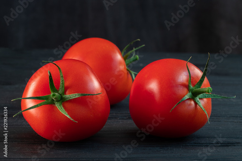 red tomatoes on a green branch on a black wooden background