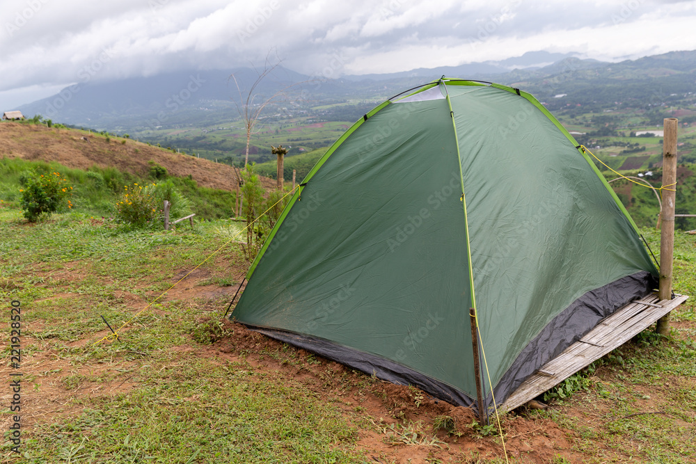 A small green tourist tent on grassy valley on mountain.