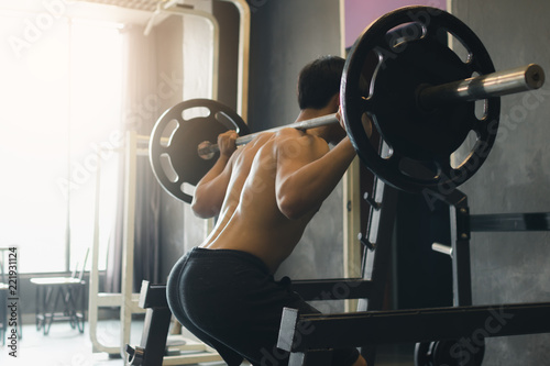 фотографія Rear view of asian man performing barbell squats at the indoor gym