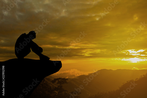 Silhouetted photo. Lonely man sitting on cliff. He is unhappy and sad. He is watching the evening glow. Photo concept for Silhouetted and depression.
