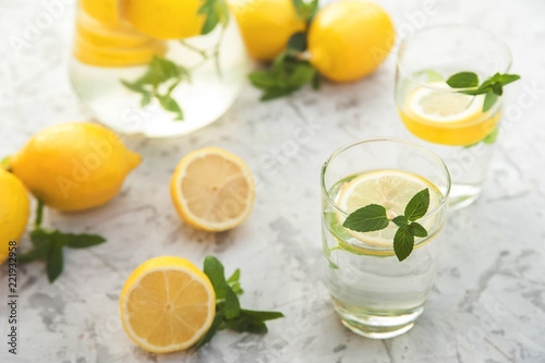 Refreshing lemonade with lemons, mint in a transparent jug and glasses on a light concrete background close-up. Background and place for text, inscriptions