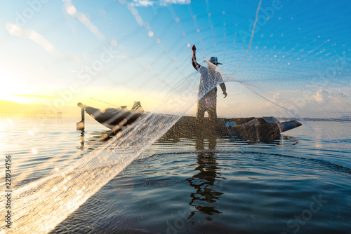 Photo shot of water spatter from fisherman while throwing fishing net on the lake. Silhouette of fisherman with fishing net in morning sunshine. Stop motion water drop.