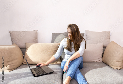 white young woman sitting on sofa behind laptop, girl in jeans with long hair