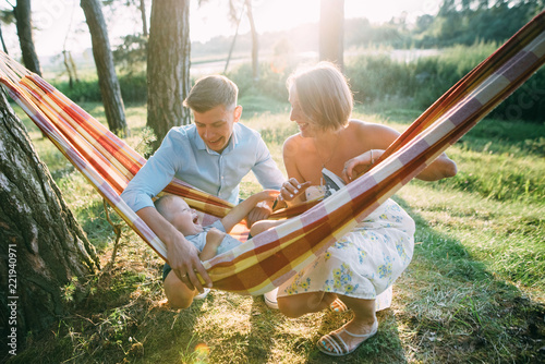Young sympathetic family - mom, dad and son rest in the nature, sitting in a hammock