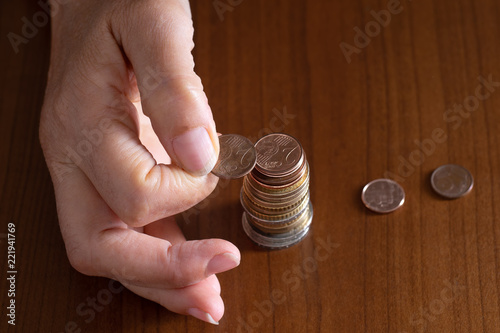 Mature woman hand putting coins into a pile on wooden table. Closeup. European euro coins, poverty concept. Counting pennies, small change.