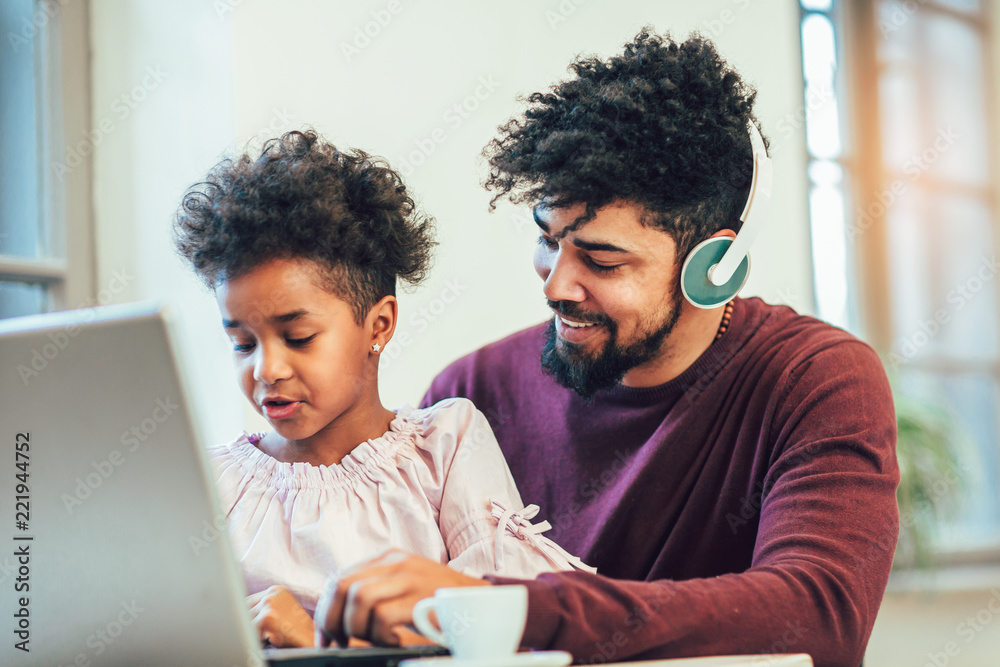 Young african american father siting together with his daughter, they are using a laptop.
