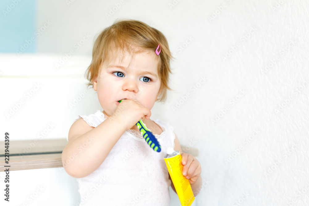 Little baby girl holding toothbrush and brushing first teeth. Toddler learning to clean milk tooth. Prevention, hygiene and healthcare concept. Happy child in bathroom.. Little baby girl holding toothbrush and brushing first teeth. Toddler learning to clean milk tooth. Prevention, hygiene and healthcare concept. Happy child in bathroom..