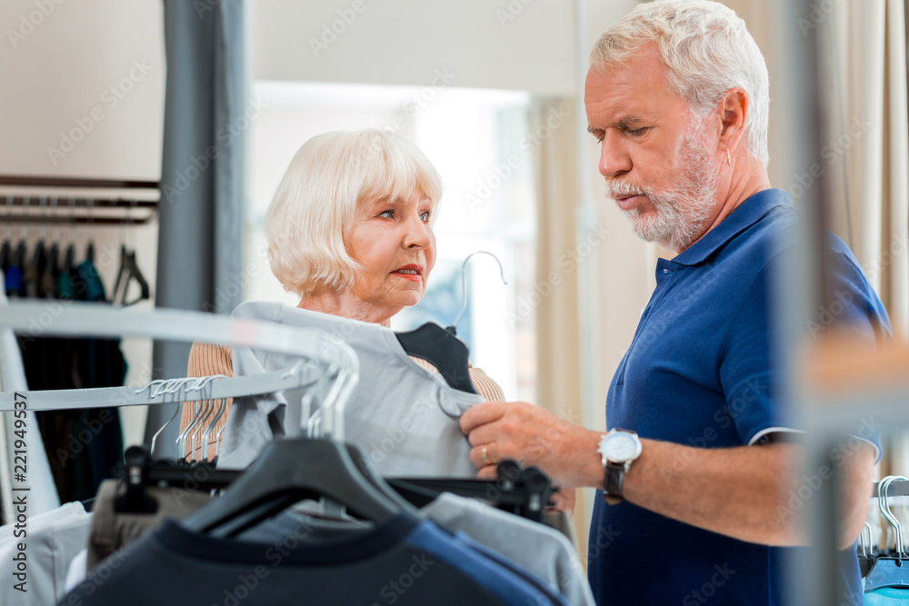 Obraz premium I doubt. Enthusiastic wonderful elderly wife suggesting a pullover while her husband expressing hesitation concerning a purchase