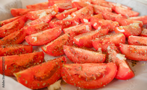 The manufacturing process of sundried tomatoes cut into slices sprinkled with salt, oregano, Basil, thyme being dried out in the sun or in the oven Close-up, selective focus.