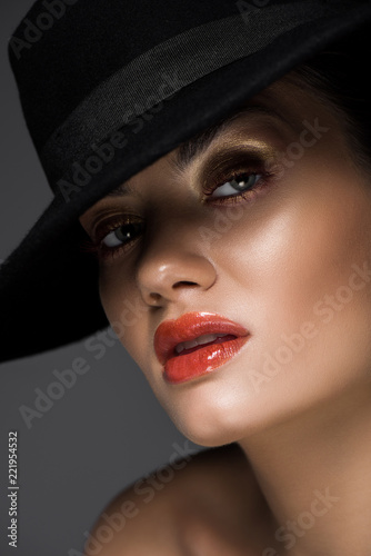 attractive girl with makeup posing in black felt hat, isolated on grey © LIGHTFIELD STUDIOS