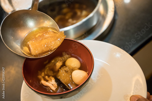 A spoon to scoop Chinese style soup; or braised fish maw in red gravy with eggs, mushroom, and bamboo shoot in white bowl. Braised Fish Maw in Red Gravy with crab in bowl.