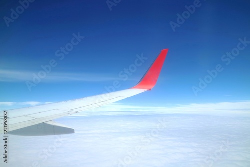 Beautiful view from airplane's window with airplane's wing, blue sky and white cloud in the summer morning. Soft focus.