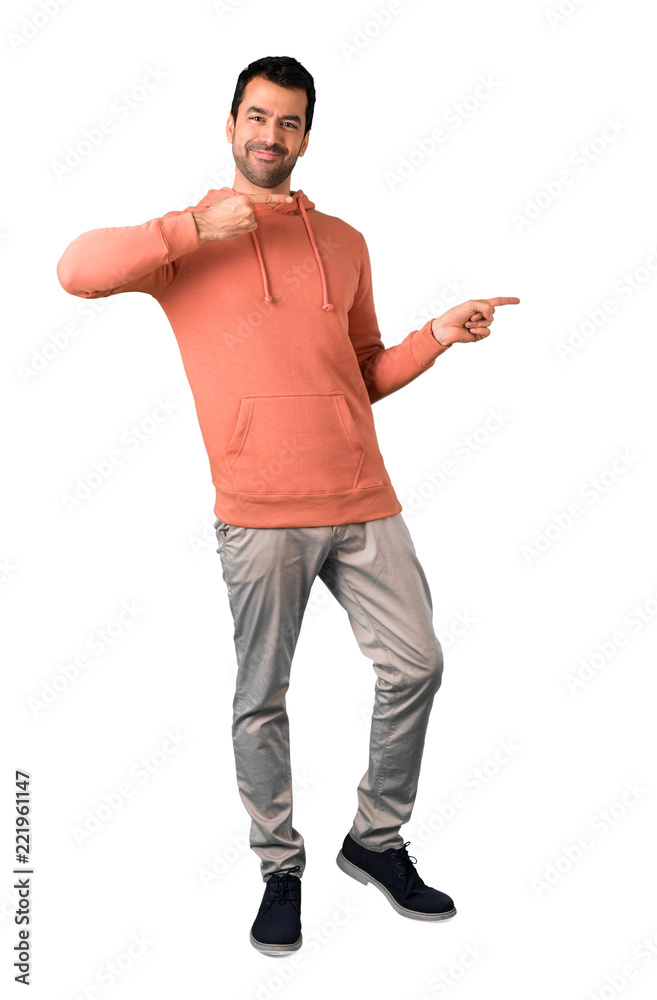 Full body of Man in a pink sweatshirt pointing finger to the side and presenting a product while smiling on isolated white background Full body of Man in a pink sweatshirt pointing finger to the side and presenting a product while smiling on isolated white background