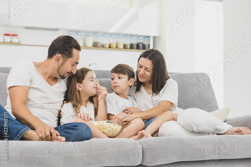 Happy young family eating popcorn while watching tv in living room