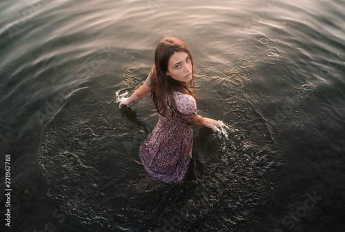 Young brunette with long hair relaxing dressed and touching water in a lake in a sunset of summer