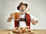Germany, Bavaria, Upper Bavaria. The senior happy smiling man with beer dressed in traditional Austrian or Bavarian costume holding mug of beer at pub or studio. The celebration, oktoberfest, festival