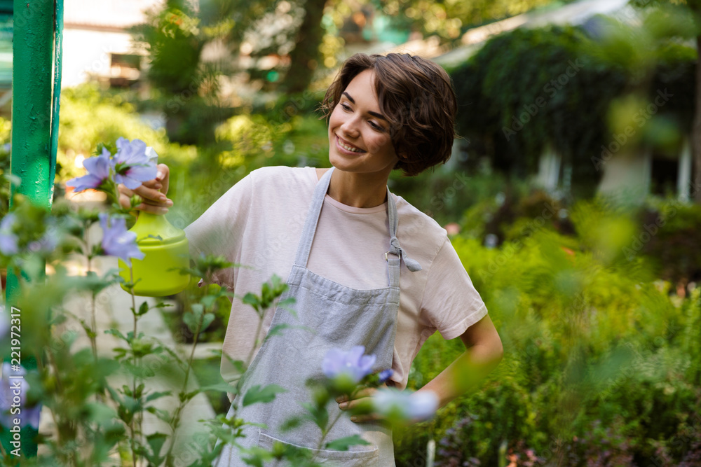 Woman gardener standing over plants in greenhouse water flowers Woman gardener standing over plants in greenhouse water flowers