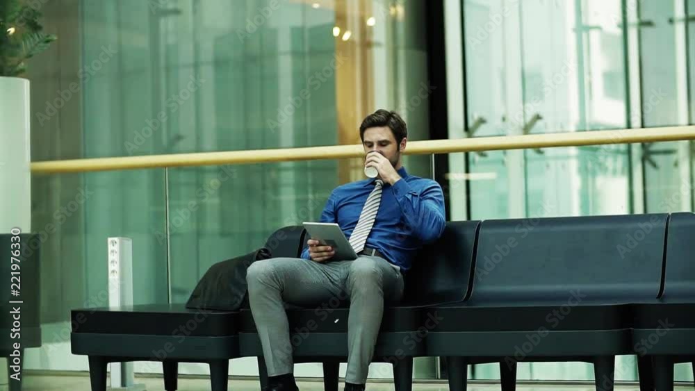 A young businessman with tablet sitting on a bench in a modern building. A young businessman with tablet sitting on a bench in a modern building.