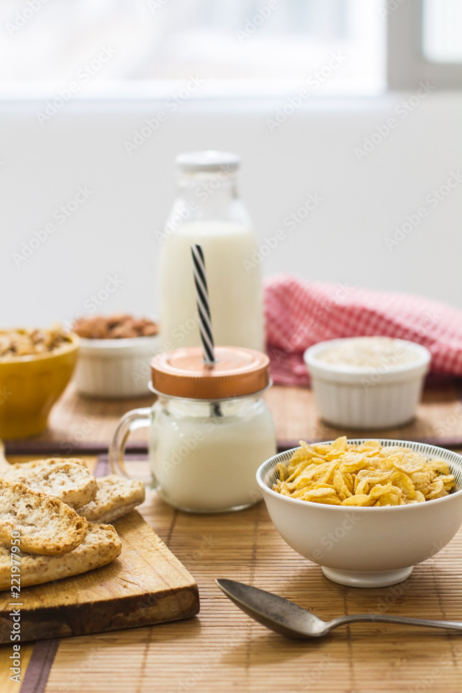 Copos de maíz, leche, tostadas y frutos secos sobre una mesa de madera en la cocina. Vista de frente Copos de maíz, leche, tostadas y frutos secos sobre una mesa de madera en la cocina. Vista de frente